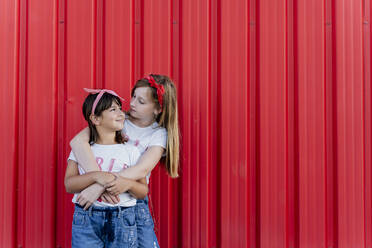 Two sisters standing in front of a red wall, face to face - ERRF01615