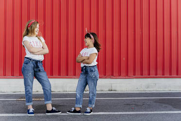 Sisters with arms crossed standing in front of a red wall - ERRF01622