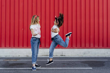 Schwestern springen auf der Straße vor einer roten Wand - ERRF01625