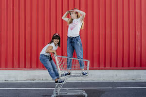 Sisters with shopping cart in front of red wall - ERRF01638