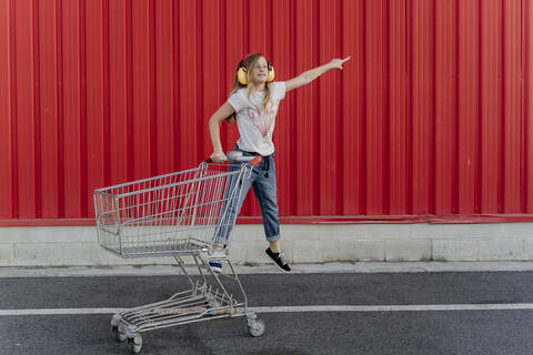 Mädchen mit Einkaufswagen und Ohrenschützer vor roter Wand, lizenzfreies Stockfoto