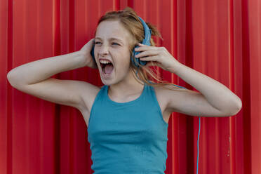 Girl with headphones in front of red wall - ERRF01661