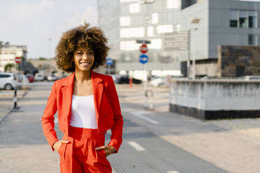 Portrait of smiling young woman wearing fashionable red pantsuit - GIOF06853