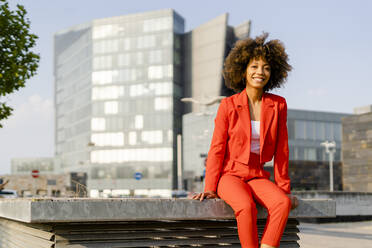 Portrait of smiling young woman wearing fashionable red pantsuit in the city - GIOF06855