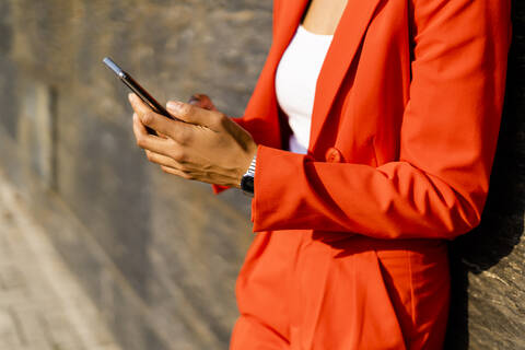 Frau in modischem roten Hosenanzug hält Handy, Teilansicht, lizenzfreies Stockfoto