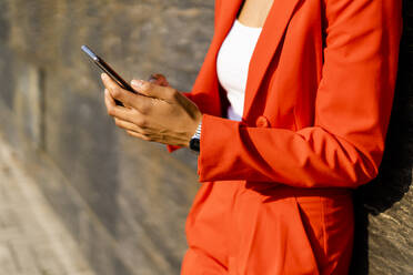 Woman wearing fashionable red pantsuit holding cell phone, partial view - GIOF06866