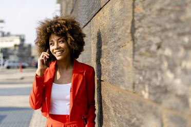 Portrait of smiling young woman on the phone wearing fashionable red pantsuit - GIOF06870