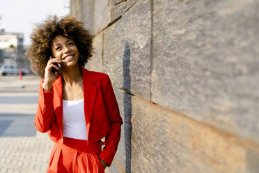 Portrait of smiling young woman on the phone wearing fashionable red pantsuit - GIOF06871