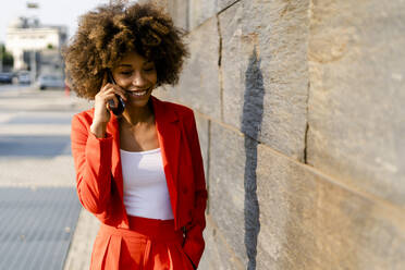 Portrait of smiling young woman on the phone wearing fashionable red pantsuit - GIOF06872
