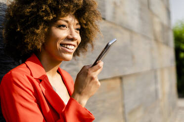 Portrait of smiling young woman on the phone wearing fashionable red suit jacket - GIOF06874