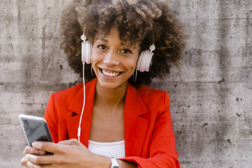 Porträt einer lächelnden jungen Frau mit Smartphone und Kopfhörern - GIOF06879