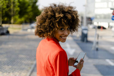 Porträt einer lächelnden jungen Frau mit Smartphone und modischer roter Anzugsjacke - GIOF06883