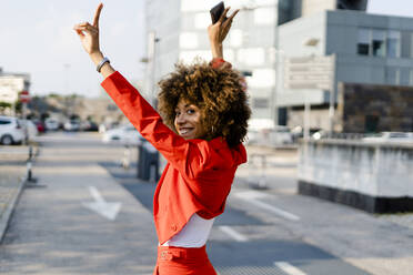 Portrait of happy young woman wearing fashionable red pantsuit showing victory sign - GIOF06886