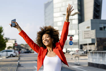 Porträt einer glücklichen jungen Frau mit Smartphone und modischer roter Anzugsjacke - GIOF06888