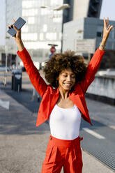 Porträt einer glücklichen jungen Frau mit Smartphone und modischem roten Hosenanzug - GIOF06889