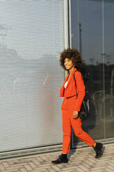 Smiling young woman with shoulder bag wearing fashionable red pantsuit - GIOF06896