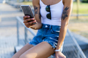 Hand of tattooed young woman holding smartphone, close-up - GIOF06909