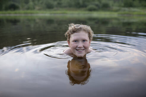 Porträt eines lächelnden Jungen, der in einem See schwimmt - VPIF01384