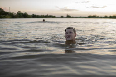 Porträt eines lächelnden Jungen, der bei Sonnenuntergang in einem See schwimmt - VPIF01398