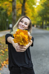 Smiling woman presenting bunch of autumn leaves - JUNF01678