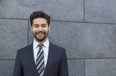 Portrait of bearded young businessman wearing blue suit jacket and tie - JUNF01688