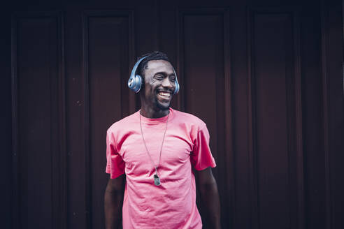 Laughing man wearing pink t-shirt listening to music with headphones - OCMF00514