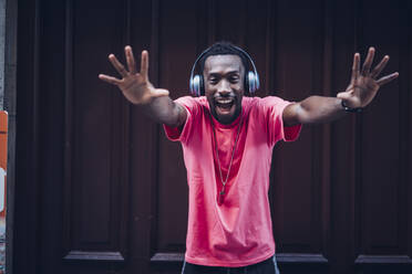 Porträt eines aufgeregten Mannes mit rosa T-Shirt, der mit Kopfhörern Musik hört - OCMF00515
