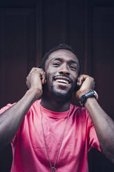 Portrait of happy man wearing pink t-shirt listening to music with headphones - OCMF00517