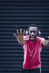 Portrait of excited man wearing pink t-shirt listening to music with headphones - OCMF00523