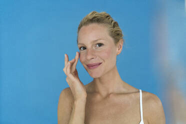 Portrait of beautiful blond woman applying eye cream - JOSF03538