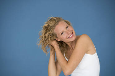 Porträt einer schönen blonden Frau, Hände im Haar, blauer Hintergrund - JOSF03549