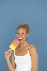 Porträt einer blonden Frau mit großem Eis am Stiel, blauer Hintergrund - JOSF03554