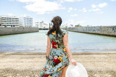 Rückansicht einer Frau mit weißem Sonnenhut am Hafen von Arrecife, Spanien - KIJF02507