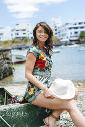 Frau mit weißem Sonnenhut sitzt auf einem Boot in Arrecife, Spanien - KIJF02516