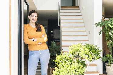 Portrait of smiling young woman leaning against terrace door - UUF18249