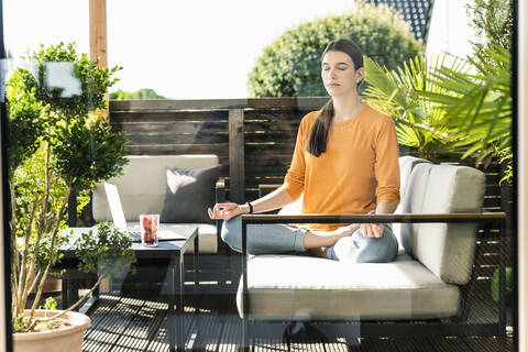 Young woman sitting on couch on terrace practicing yoga stock photo