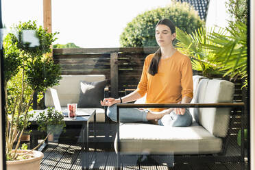 Junge Frau sitzt auf der Couch auf der Terrasse und übt Yoga - UUF18260