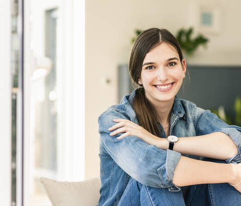 Porträt einer lächelnden jungen Frau, die zu Hause ein Jeanshemd trägt, lizenzfreies Stockfoto