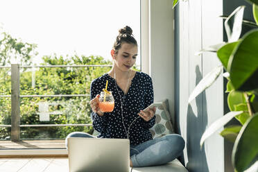 Smiling young woman with laptop, cell phone and healthy drink at home - UUF18274