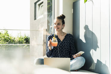 Smiling young woman with laptop, cell phone and healthy drink at home - UUF18275