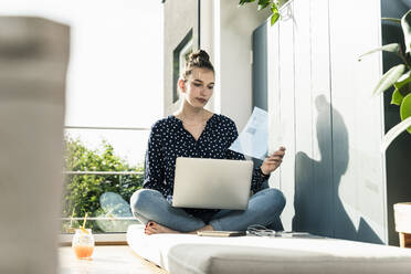 Young woman at home with laptop and transparent document - UUF18276