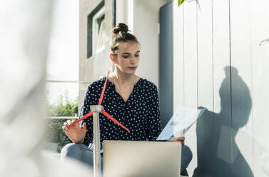 Young woman at home with wind turbine model and transparent document - UUF18277