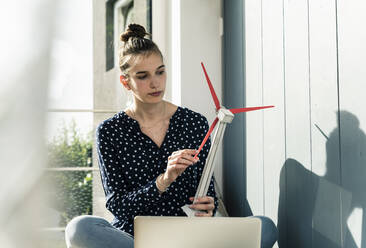 Young woman at home holding wind turbine model - UUF18279