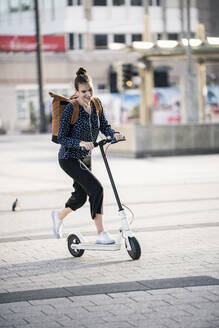 Junge Frau fährt Elektroroller in der Stadt - UUF18287