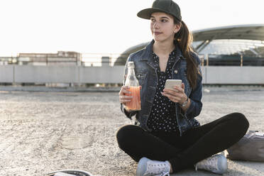 Junge Frau mit Getränk und Mobiltelefon auf dem Parkdeck bei Sonnenuntergang - UUF18313