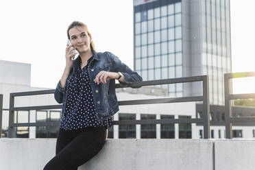 Smiling young woman on cell phone standing on parking deck - UUF18317