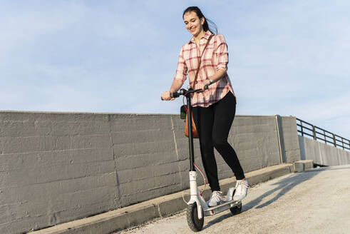 Young woman riding electric scooter on parking deck - UUF18318