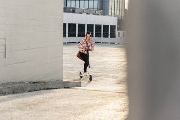 Junge Frau mit Kopfhörern auf einem Elektroroller auf einem Parkdeck - UUF18323