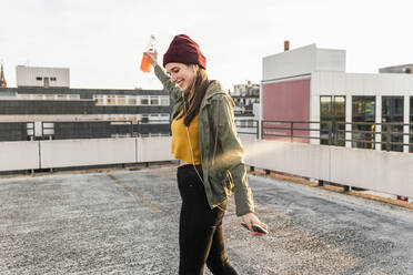 Happy young woman with earphones dancing on parking deck - UUF18331