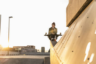 Stylische junge Frau mit Skateboard auf Parkdeck - UUF18336